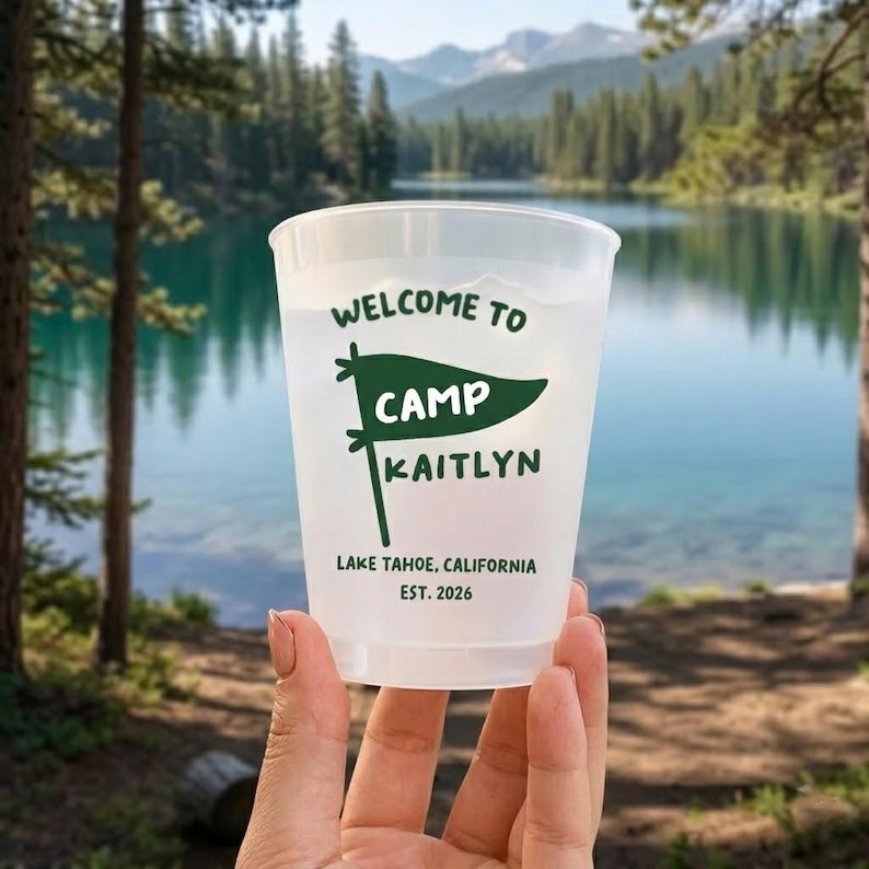 May include: A translucent plastic cup featuring dark green text and a pennant graphic. The text reads: WELCOME TO CAMP KAITLYN, LAKE TAHOE, CALIFORNIA, EST. 2026. The design includes a pennant icon with the word CAMP inside and KAITLYN below it.