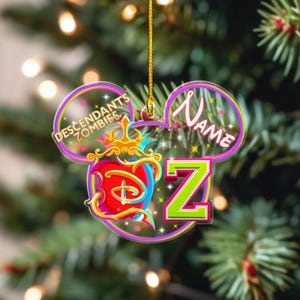 May include: A clear acrylic Christmas ornament shaped like Mickey Mouse ears. The ornament has the text "Descendants Zombies" and "Name", a letter "Z", and a colourful design with a crown and the Disney logo. It hangs from a gold string.
