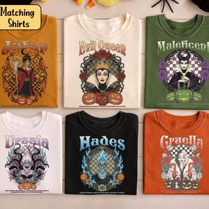 May include: Six Halloween-themed t-shirts are displayed. Each shirt showcases a different Disney villain: Jafar, Evil Queen, Maleficent, Ursula, Hades, and Cruella. The shirts are in various colours, with detailed graphic designs and text.