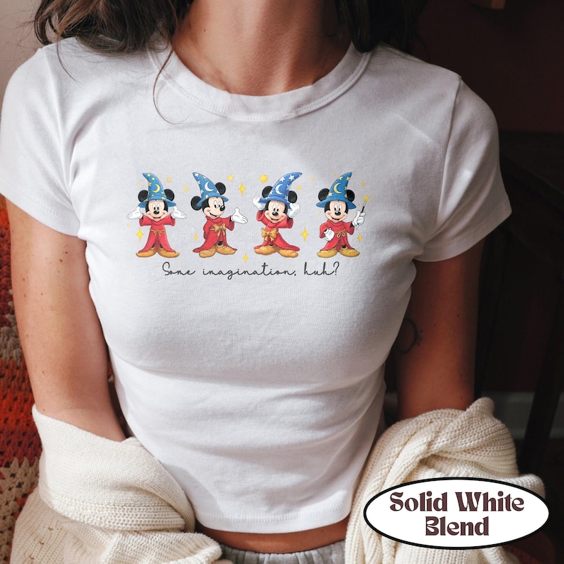 May include: White t-shirt featuring a graphic of Mickey Mouse dressed as a sorcerer, with the text "Some imagination, huh?" The design includes Mickey in red robes and blue wizard hats. The shirt has a "Solid White Blend" label.