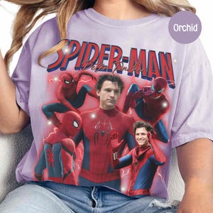 May include: A light purple t-shirt featuring a graphic of Spider-Man with the text "SPIDER-MAN Peter Parker" in red. The design includes multiple images of Spider-Man in his costume, with lightning bolt accents.