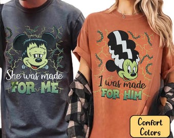 May include: Two t-shirts, one gray and one orange, featuring a cartoon character design. The design depicts a Frankenstein-themed mouse with the text "She was made FOR ME" and "I was made FOR HIM". The shirts are labeled "Comfort Colors".