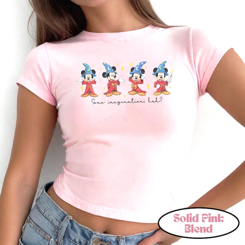 May include: A light pink t-shirt with a crew neck and short sleeves. The shirt features a graphic of Mickey Mouse dressed as a wizard with the text "Some imaginations, huh?" The shirt is labeled "Solid Pink Blend".