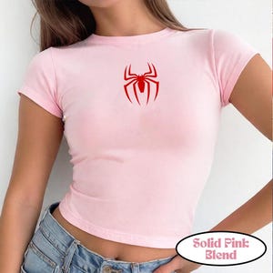 May include: A light pink, short-sleeved t-shirt with a red spider graphic on the front. The shirt has a crew neck and is made of a soft material. The text "Solid Pink Blend" is in a white oval at the bottom.