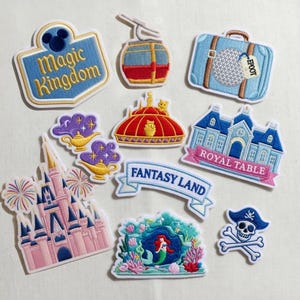 May include: Embroidered patches featuring various designs, including a castle, a suitcase with "EPCOT" tag, a pirate skull, and text that reads "Magic Kingdom" and "Fantasy Land". The patches are in various colors, including blue, pink, and red.