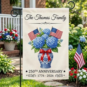 May include: A beige garden flag features the text "The Thomas Family" above a blue and white vase filled with blue hydrangeas and two American flags. The flag also displays "250th Anniversary 1776-2026".