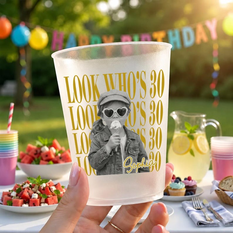 May include: A frosted plastic party cup featuring the gold text "LOOK WHO'S 30" repeated in the background. The center displays a black and white photograph of a child wearing a cap and heart-shaped sunglasses while eating ice cream, with the name "Sophia" in gold script.