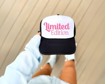 May include: A black and white trucker hat with a white front panel and a pink cursive inscription that reads "Limited Edition".