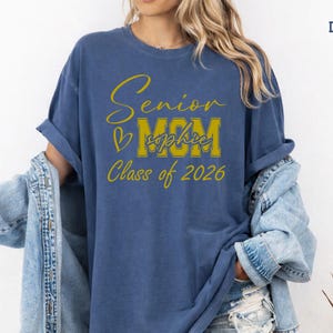 Custom Senior Mom Comfort Colors® shirt displayed in blue jean with a bold white MOM design, elegant Senior script and Class of 2026 text. Add the graduate’s name for a personal touch that makes this tee perfect for proud moms, graduation season, senior night, school memories, family photos and thoughtful graduate mom gifts.