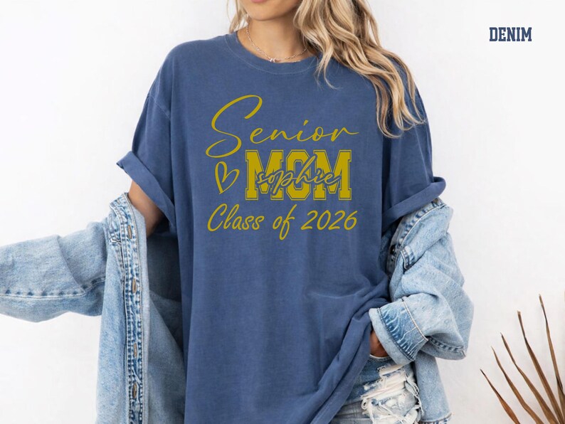 Custom Senior Mom Comfort Colors® shirt displayed in blue jean with a bold white MOM design, elegant Senior script and Class of 2026 text. Add the graduate’s name for a personal touch that makes this tee perfect for proud moms, graduation season, senior night, school memories, family photos and thoughtful graduate mom gifts.