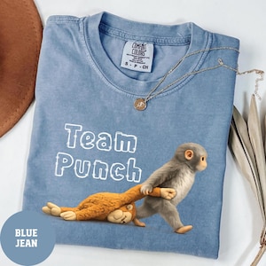 May include: Blue jean colored t-shirt with the text "Team Punch" in white. The shirt features a cartoon monkey pulling another cartoon monkey. A gold necklace with a pendant is on the shirt.