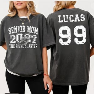 two people wearing gray t-shirts with text and numbers printed on them.