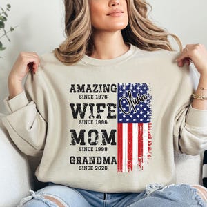 A woman wearing a beige sweatshirt with a graphic design featuring text and an American flag.