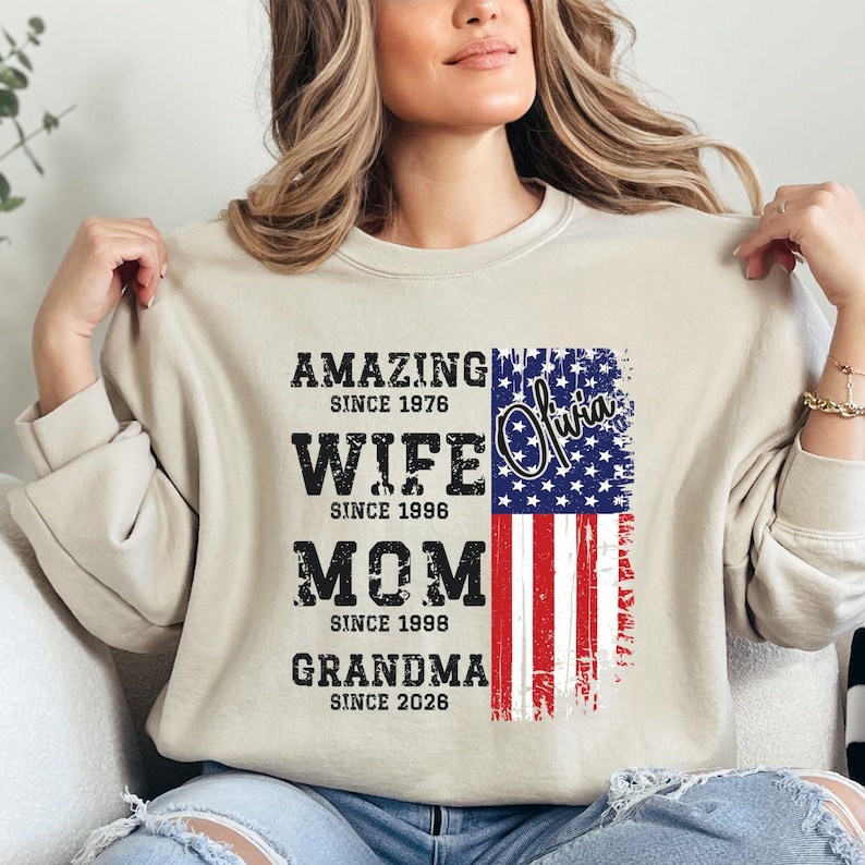 A woman wearing a beige sweatshirt with a graphic design featuring text and an American flag.