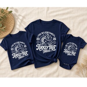 three navy blue t-shirts with a white turkey trot design, arranged on a beige surface.