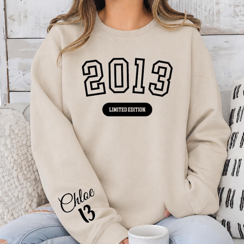 A woman wearing a beige sweater with the text "2013" and "LIMITED EDITION" printed on it.