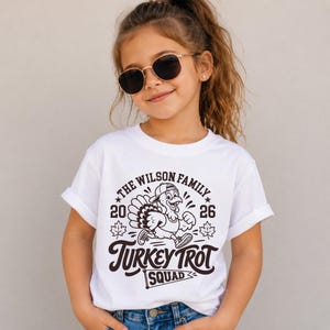 Personalized family Turkey Trot shirts shown in a Thanksgiving holiday mockup. Matching cream shirts include a vintage athletic turkey graphic, “Turkey Trot Squad,” family name, and 2026 year design. Coordinating adult and baby apparel makes a fun Thanksgiving outfit for families who run together, attend local Turkey Trot events, celebrate Thanksgiving Day, or want matching holiday family photos.