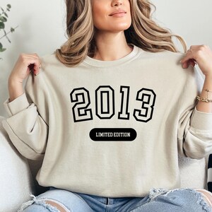 A woman wearing a beige sweater with the text "2013" and "LIMITED EDITION" printed on it.