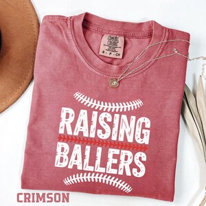 Show your sports mom pride with this Raising Ballers Comfort Colors® t-shirt. Designed with a classic baseball inspired graphic, this relaxed fit tee is perfect for baseball games, softball tournaments, and weekend practices. The soft garment dyed fabric gives it a vintage look and feel that sports moms love. A perfect gift for baseball and softball moms.