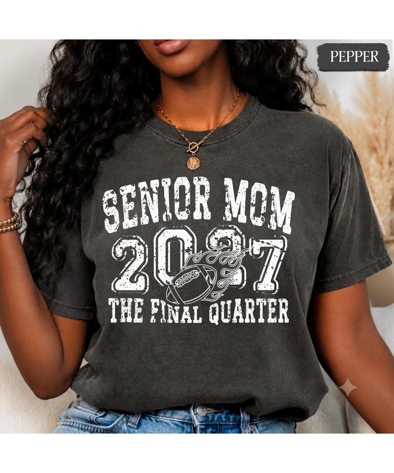 A woman wearing a black t-shirt with white text and graphics, including the text "SENIOR MOM 2007 THE FINAL QUARTER".