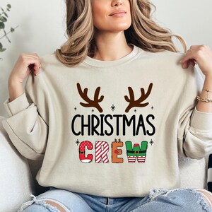 cute christmas crew sweatshirt with reindeer antlers and personalized sleeve name option, matching holiday family sweater for kids and adults, custom christmas shirt for winter celebrations, cozy xmas crew top with festive lettering, personalized holiday gift sweatshirt, christmas pajamas top for family photos, fun reindeer themed christmas sweater, holiday party outfit idea, custom name christmas crew shirt, adorable winter sweatshirt for holiday season
