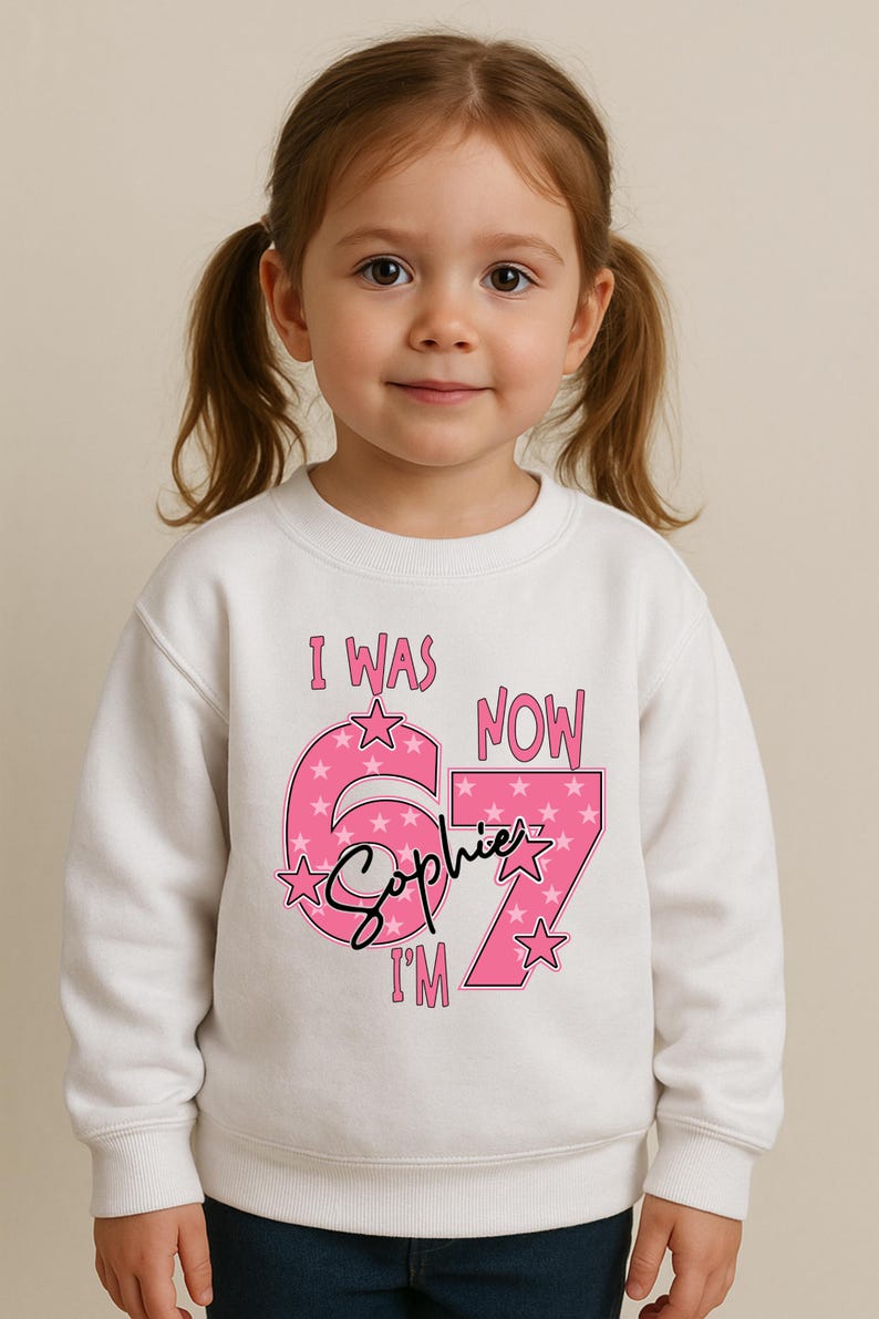 A young girl wearing a white sweatshirt with a pink and purple design and text on it.