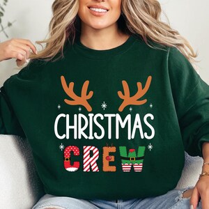 cute christmas crew sweatshirt with reindeer antlers and personalized sleeve name option, matching holiday family sweater for kids and adults, custom christmas shirt for winter celebrations, cozy xmas crew top with festive lettering, personalized holiday gift sweatshirt, christmas pajamas top for family photos, fun reindeer themed christmas sweater, holiday party outfit idea, custom name christmas crew shirt, adorable winter sweatshirt for holiday season