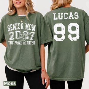 A woman wearing a green t-shirt with text and numbers printed on it.