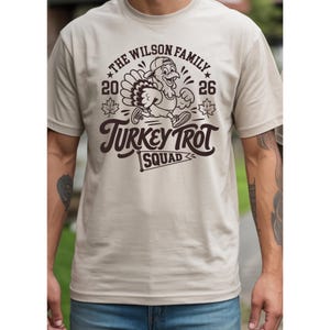 Thanksgiving 2026 matching family shirt set with a vintage Turkey Trot theme. The cream adult and baby shirts feature a running turkey illustration surrounded by autumn leaves and bold retro lettering. The design can be personalized with a family name and is ideal for Thanksgiving morning Turkey Trot races, family reunions, holiday photos, November gatherings, and festive family traditions.