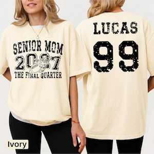 A woman wearing a white t-shirt with text and numbers printed on it.