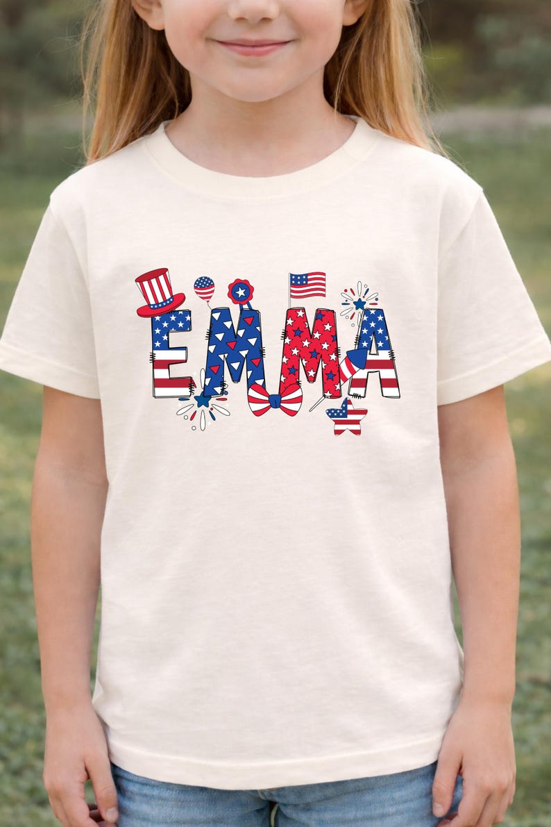 A front-facing outdoor mockup shows a child wearing a natural cream personalized patriotic T-shirt with the custom name Emma printed across the chest. The design features red, white, and blue colors, stars, stripes, fireworks, and festive Americana elements for a playful holiday look. This custom kids shirt is designed for Fourth of July celebrations, matching family outfits, summer events, and the 250th anniversary of America in 2026.