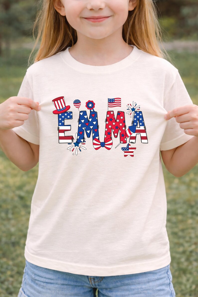 A young girl wears a white personalized patriotic sweatshirt featuring the custom name Emma in large red, white, and blue letters decorated with stars, stripes, fireworks, and a festive patriotic bow. The clean studio background keeps the focus on the custom front design and comfortable fit. This mockup presents a personalized kids sweatshirt perfect for Fourth of July parties, family gatherings, parade outfits, and America 250 celebration apparel.