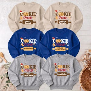 May include: Six long-sleeve crewneck sweatshirts in beige, blue, and gray. Each features a graphic with a cookie, a Santa hat, and the text Cookie Crew. Below, a rolling pin graphic displays titles: Quality Control, Sprinkle Specialist, Head Baker, Official Cookie Tester, Chief Taste Tester, and Dough Roller.