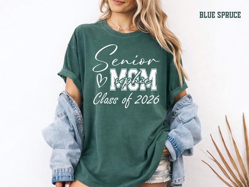 Senior Mom Class of 2026 Comfort Colors® tee in a soft blue jean shade with white personalized graduation design. This custom shirt is a stylish way for moms to celebrate their senior graduate with name personalization, school spirit style and meaningful keepsake details for graduation day, senior night, family photos and parties.