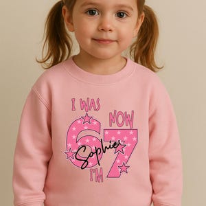 A young girl wearing a pink sweatshirt with a personalized message and stars on it.