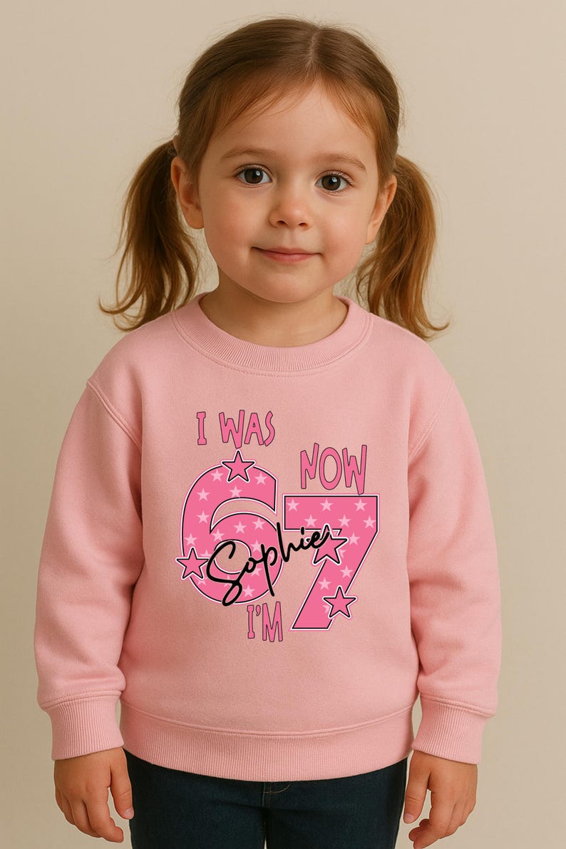 A young girl wearing a pink sweatshirt with a personalized message and stars on it.