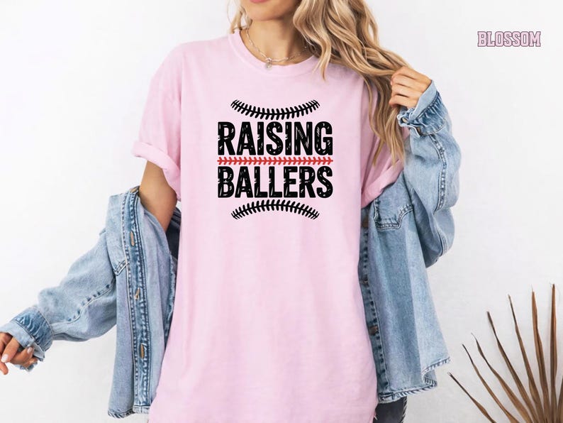 This Raising Ballers Comfort Colors® tee is the perfect game day shirt for sports moms who proudly support their kids on the field. Featuring a classic baseball inspired design and soft garment dyed fabric, this shirt combines comfort and style for baseball season, softball tournaments, and everyday wear.