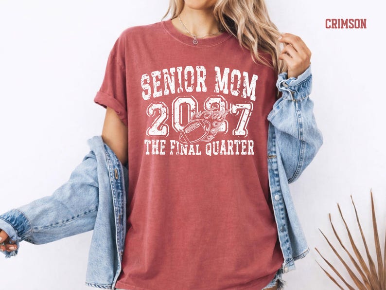 A woman wearing a red t-shirt with the text "SENIOR MOM 2007 THE FINAL QUARTER" printed on it, along with a denim jacket.