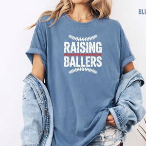 Life at the ball field means raising future athletes. This Raising Ballers Comfort Colors® shirt celebrates the busy but rewarding life of a sports mom. The vintage baseball design and comfortable relaxed fit make it perfect for game day outfits, team events, and casual everyday wear. A great gift for baseball moms and softball moms.