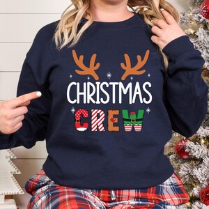 cute christmas crew sweatshirt with reindeer antlers and personalized sleeve name option, matching holiday family sweater for kids and adults, custom christmas shirt for winter celebrations, cozy xmas crew top with festive lettering, personalized holiday gift sweatshirt, christmas pajamas top for family photos, fun reindeer themed christmas sweater, holiday party outfit idea, custom name christmas crew shirt, adorable winter sweatshirt for holiday season