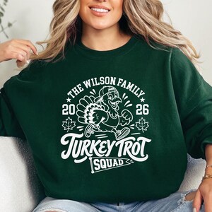 A woman wearing a green sweatshirt with a white graphic design featuring a turkey and the text "The Wilson Family Thanksgiving Trot Squad" printed on it.