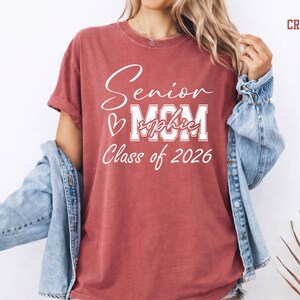 Comfort Colors® Class of 2026 mom shirt with a soft vintage blue jean look and clean white print. The design highlights Senior, MOM, custom name text and Class of 2026 wording for a proud graduation mom style. Great for senior night, graduation day, family photos, school spirit outfits and personalized gifts for moms of graduates.