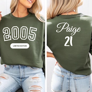 A woman wearing a green sweatshirt with the number "2005" and the name " Paige 21" printed on it.