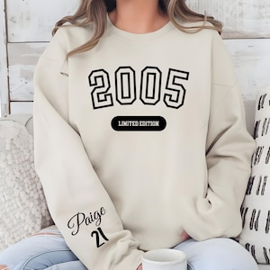 A person wearing a white sweatshirt with the number "2005" printed on it, along with the text "LIMITED EDITION" and the name " Paige 21" printed on the sleeve.