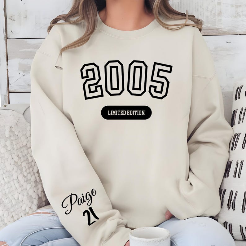 A person wearing a white sweatshirt with the number "2005" printed on it, along with the text "LIMITED EDITION" and the name " Paige 21" printed on the sleeve.