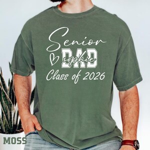 Comfort Colors® blue jean senior mom tee with white Class of 2026 artwork, heart detail and personalized name design. This soft casual graduation shirt is made for moms who want a meaningful senior year keepsake. Wear it to graduation ceremonies, senior events, school spirit days, family parties, photo sessions and Class of 2026 celebrations.