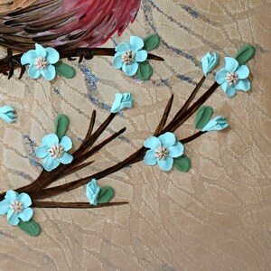 Close up of 3d hand sculpted flowers in robin egg blue on painting of red finch bird with impasto textured copper feathers on a branch