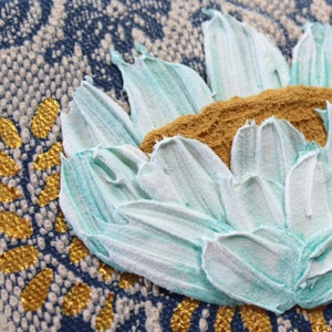 Close up of miniature painting in art deco style with a blue impasto flower on a textured background with golden leaves