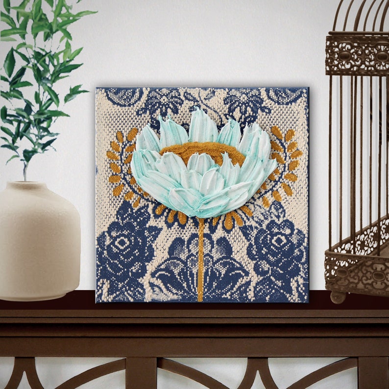 Setting view of miniature painting in art deco style with a blue impasto flower on a textured background with golden leaves