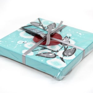 Packaging view of painting on mini canvas with 3d flower in red, black, and aqua for easy gift giving